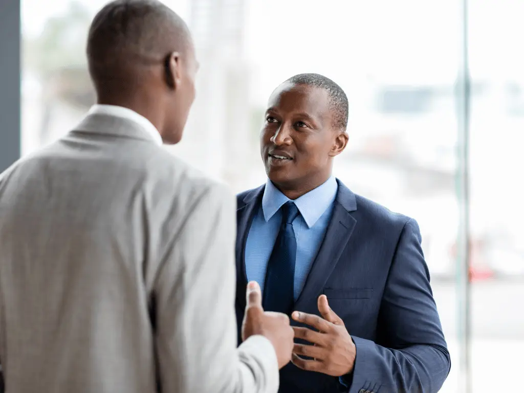 Kazicloud_Two professional men engaged in a career coaching discussion, dressed in business suits, in a modern office setting
